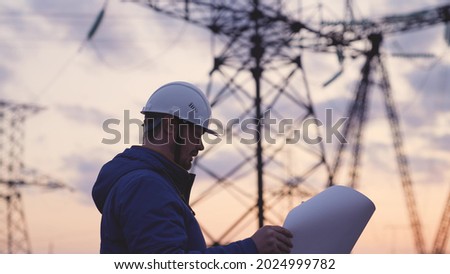 An electrician on the background of high towers of power plants looks at the project for the development of an electrical structure, the expansion of the electrical voltage of volts in the wires Foto d'archivio © 