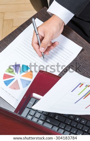 Hand of a businessman about to write on a sheet a pie chart next to a laptop