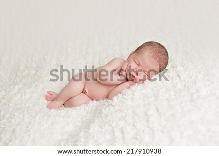 A beautiful newborn baby holds its face in its hands with feet crossed