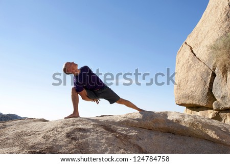 Man in yoga pose bound lunge outdoors in a spectatcular stone landscape.