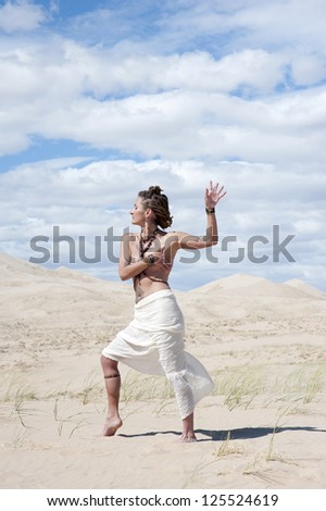 Beautiful alternative woman in a classical grecian stylesarong moving in desert dunes.