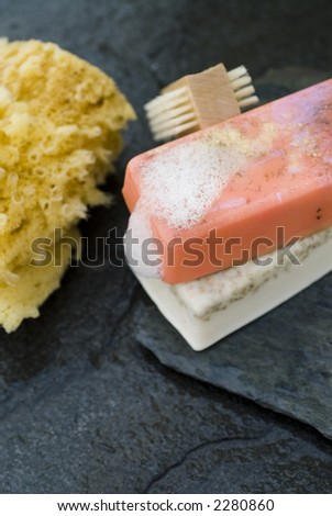 Organic soaps and sea sponge with brush on wet grey slate.