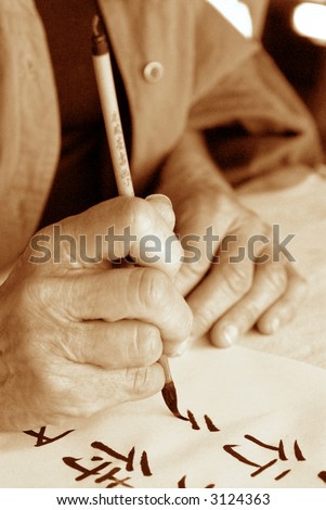 The hands of an elder person writing Chinese calligraphy. High ISO black and white sepia image.