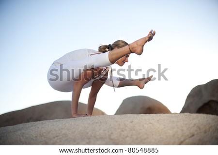 Woman in Titibasana or Firefly yoga posture in a natural boulder landscape.