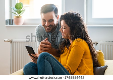 Cheerful couple using mobile phone at home stock photo