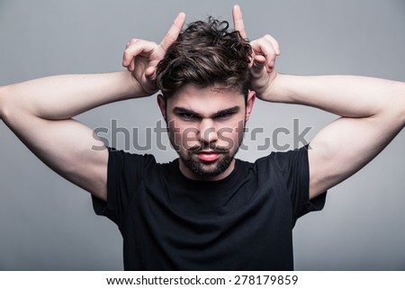 Young man in  black T-shirt with fashionable hairstyle shows hor