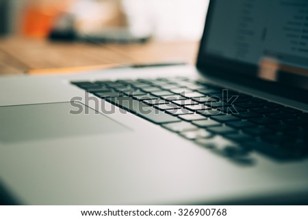 Workplace with open laptop on modern wooden desk, angled notebook on table in home interior, filtered image, soft focus