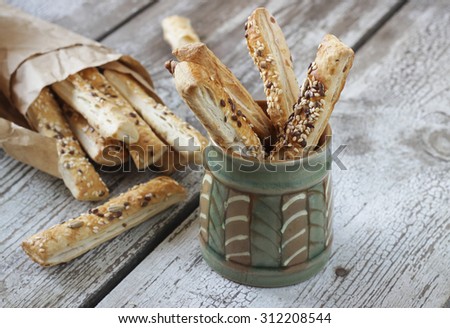 Puff pastry sticks with sesame seeds in a paper bag and ceramic bowl