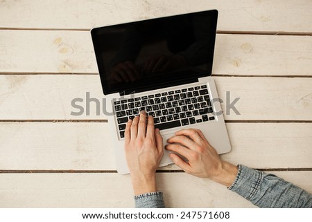 Man\'s hands typing on laptop keyboard on the wooden floor