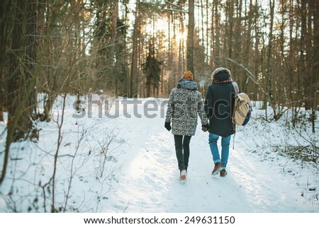 Young hipster couple having a walk in winter forest with bag alone