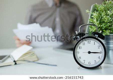 Busy man with papers over the table with alarm clock and laptop
