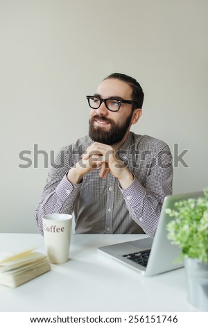 Busy man with beard in glasses thinking over laptop with coffee on the table