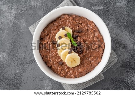 Chocolate oatmeal porridge with banana and chocolate chips on top in a white bowl. Healthy breakfast. Copy space Photo stock © 