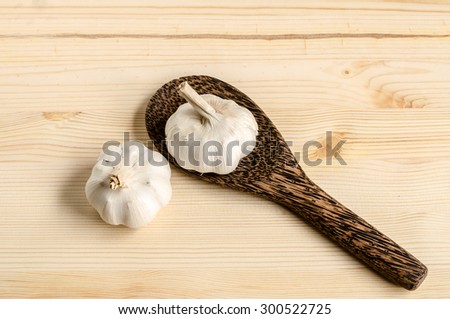 Serving spoons and two garlics on wooden surface