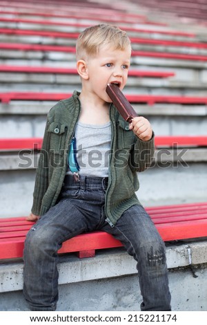 Blonde boy eating chocolate ice cream outside