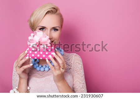 Happy birthday. Sweet blonde woman holding small gift box with ribbon. Soft colors. Studio portrait over pink background