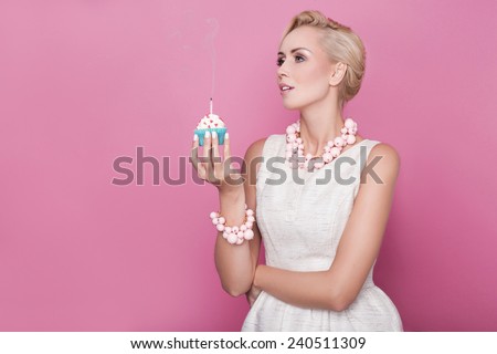 Beautiful women with cream dress holding small cake with colorful candle. Birthday, holiday. Studio portrait over pink background