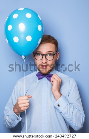 Attractive young man with a blue balloon in his hand. Party, birthday, Valentine. Studio portrait over blue background