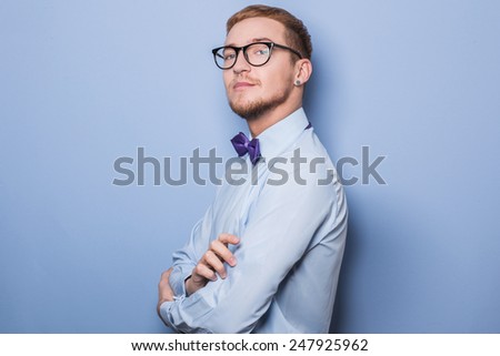 Young fashion male model wearing bow tie and blue shirt. Studio portrait over blue background