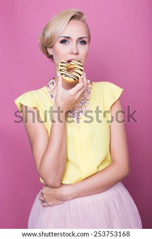 Beautiful blonde women with yellow blouse taste yellow dessert. Fashion shot. Soft colors. Studio portrait over pink background