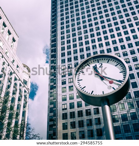 LONDON, UK - 27 APRIL 2015: A low angle view of one of the clocks located at the base of Canary Wharf tower (in the background, left) and the Reuters building (right) on a bright spring morning.