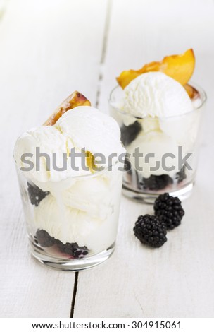Ice cream in glass with a peach and blackberry on a white wooden background