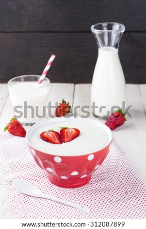 Semolina strawberry in red bowl on fabric napkin on a white table with milk and a white ceramic spoon
