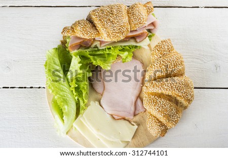 Ingredients for a sandwich: croissant with sesame, lettuce, cheese, ham on a white wooden background