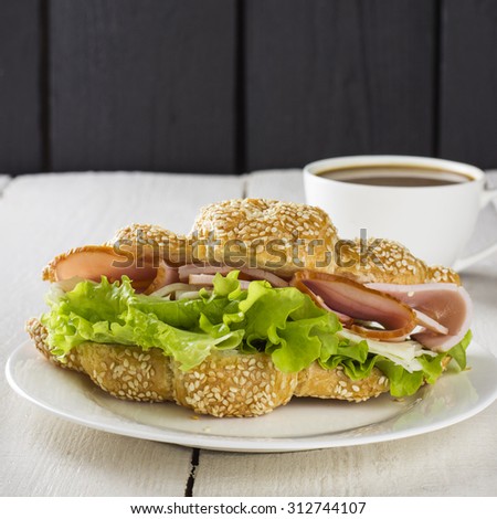 Sandwich with lettuce, ham, cheese and cup of coffee on a white wooden background