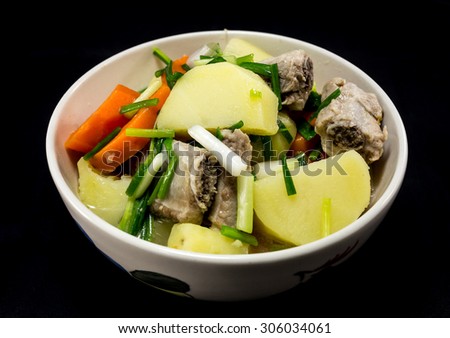 Detail of bowl with potato soup with pork rib and carrot on black background. Vietnam food