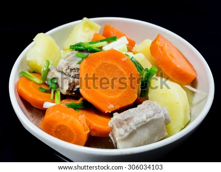 Detail of bowl with potato soup with pork rib and carrot on black background. Vietnam food
