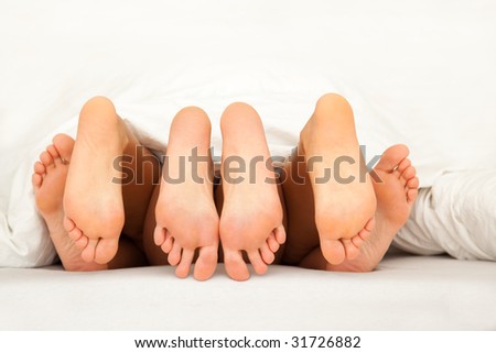 Three pairs of feet having fun in the bed having a threesome