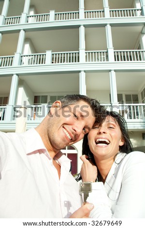 Key holding smiling hapy couple in front of new real estate balcony residential house