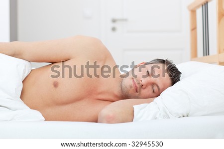 Cheerful man lying in bed and having sweet dreams while sleeping
