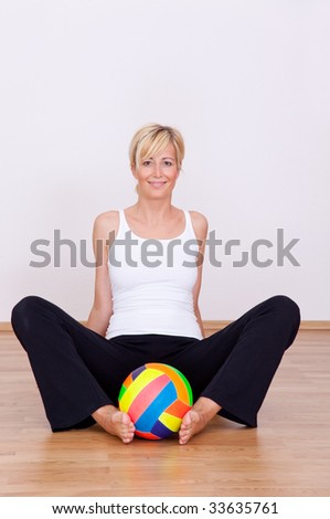 Smiling fitness woman sitting on wooden floor with colorful ball at home after beginning training excercises