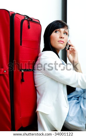 Business woman sitting on airport and phoning while waiting with luggage