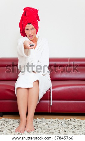 Channel switching female in bathrobe towel sitting in living room on red leather couch