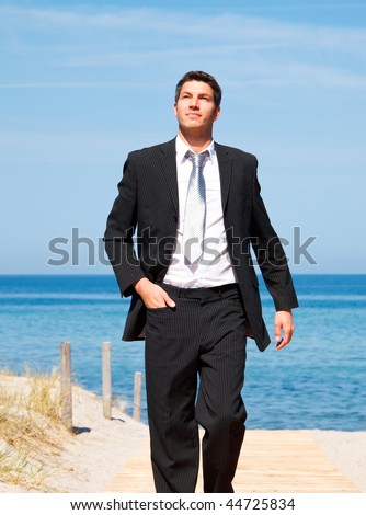 Carefree successful businessman walking with success on boardwalk on coastline with blue sky and sea wearing tie and formal clothes
