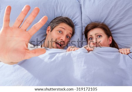 scared couple in bed making hand stop symbol