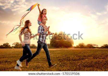 Photo of family running through field letting kite fly