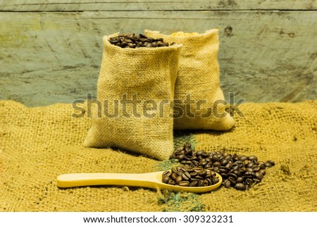 coffee beans in sack bag and spoon on roasted coffee seed background.