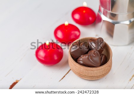 Chocolate candies in wood bowl, candles, coffee maker on white wood background