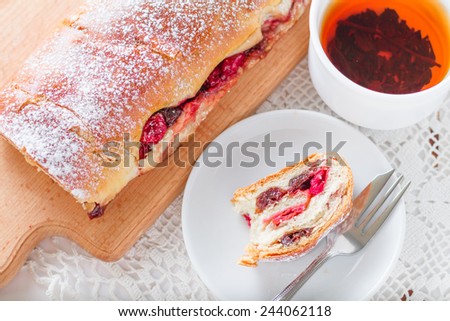 Cherry roll on white plate and wood board, black tea on white knitted tablecloth, top view