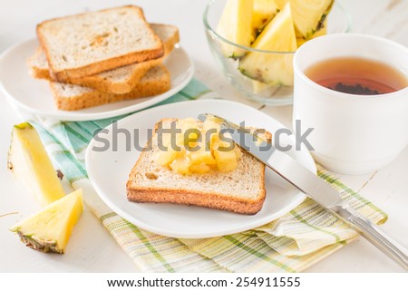 Breakfast - toast, pineapple jam, pineapple slices, tea, plaid napkin, white wood background