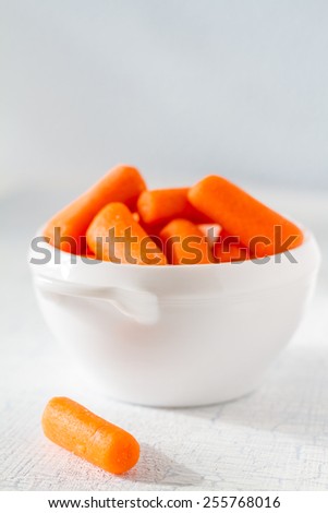 Baby carrot sticks in white bowl on light blue wood background, closeup