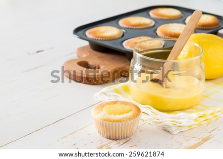 Lemon cupcakes preparation - cupcakes in forms, curd, lemon on white wood background