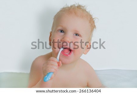 Toddler boy brushing his teeth in bathtub, smiling, light grey background