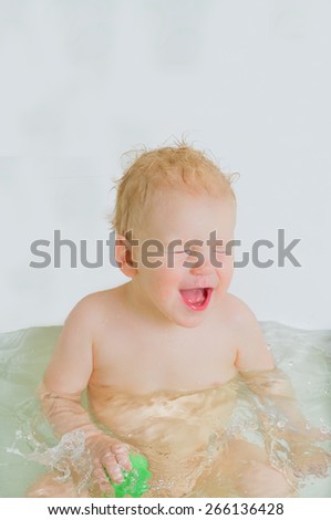 Toddler boy playing in bathtub, smiling, light grey background