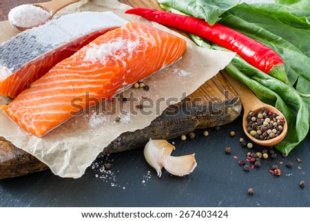 Salmon fillet with spinach salt, pepper, garlic, oil, dark stone background, closeup