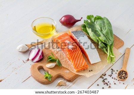 Salmon fillet with spinach, salt, pepper, garlic, oil, white wood background